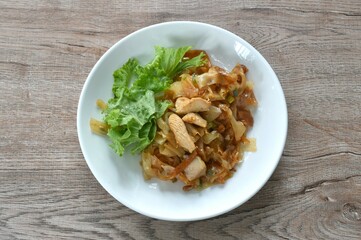 spicy fried large rice noodles with chicken and slice lettuce on plate 