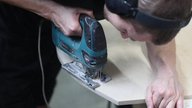 An experienced pasteur carpenter carefully makes a figured cut on a wooden slab with an electric tool. Material Cutting Process in Furniture Production
