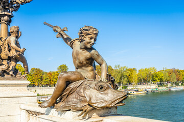 Bronze statue of a genius on a fish and holding a trident spear of Pont Alexandre III bridge in...