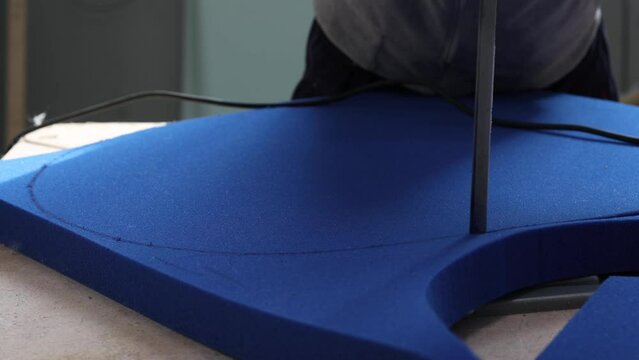 In the production of furniture, the craftsman uses equipment to cut a round piece from thick blue foam rubber. The Process of Manufacturing Parts in Furniture Production