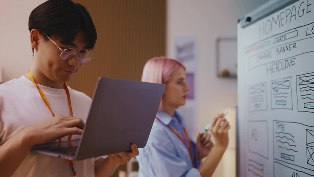 Web developers working on website design, woman colleague writing on whiteboard