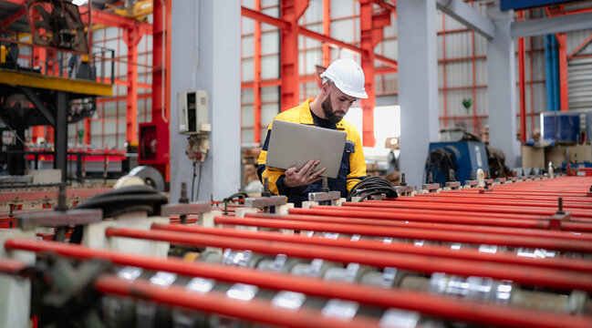 Industrial engineer in safety helmet uniform jacket working in heavy steel engineering factory. Technician manager worker inspector using laptop in metalwork product manufacturing facility workplace