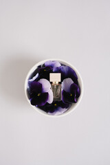 Perfume bottle in bowl with purple pansy flowers