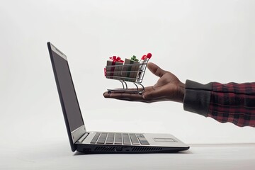A man's hand holds a small shopping cart full of goods against the background of a laptop. The concept of online shopping.