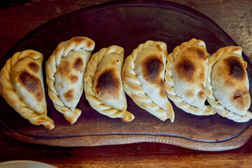 half a dozen of empanadas salteñas on a wooden board, filled with beef or llama meat, onion, potato, chili and spices. view from top
