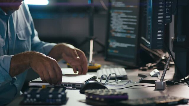 Close up of male electronics engineer taking laptop to pieces for repair with low key lighting - shot in slow motion