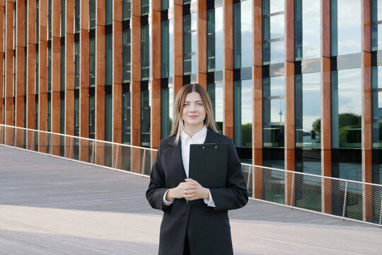 Businesswoman in a black suit with a folder in her hands in front of office building