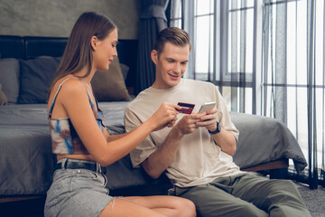 Young couple sit in the home bedroom using online payment app and digital wallet on smartphone to...