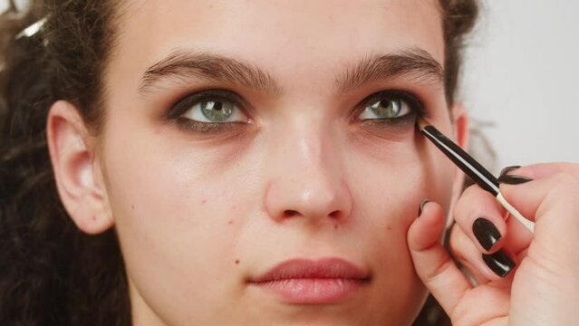 Eye shadow makeup to the upper eyelid, close-up. Makeup artist applies a bright eye shadow with a make-up brush.Tutorial master class of professional makeup, smoky eyes 
