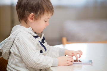 Baby plays with a mobile phone while sitting at the table. The child looks at the phone screen. Kid aged two years