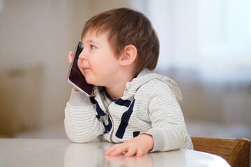 Baby is talking on a mobile phone. A curious child is calling on the phone. Kid aged two years