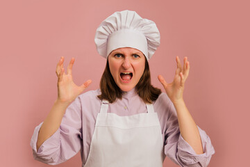Furious woman cook on studio pink background. Portrait of a female person in chef's clothing
