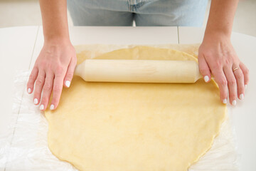 Closeup on female hands rolling dough with rolling pin on white background. Process of cooking pecan pie in home kitchen for American Thanksgiving Day.