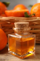 Bottle of tangerine essential oil and fresh fruits on wooden table, closeup