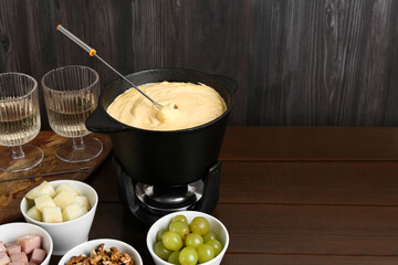 Fondue pot with tasty melted cheese, forks, wine and different snacks on wooden table, space for text