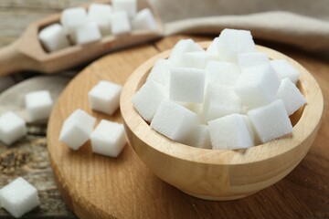 White sugar cubes in bowl and scoop on wooden table, closeup