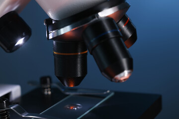 Microscope with glass slide on blue background, closeup
