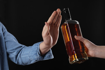 Alcohol addiction. Man refusing bottle of whiskey on black background, closeup