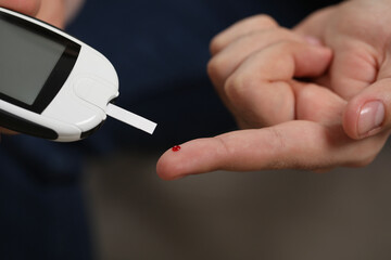 Diabetes test. Man checking blood sugar level with glucometer on blurred background, closeup