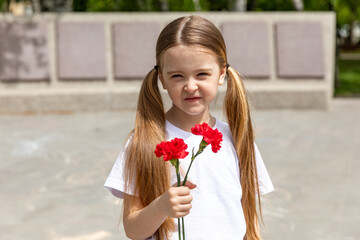 Victory Day concept. Little girl with two red carnations at the Eternal flame near the monument of Unknown soldiers tomb. 9 May celebration