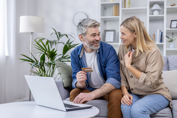An affectionate mature couple enjoys a moment of online shopping in their cozy living room, illustrating love, technology, and consumerism.