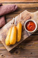 Corn dogs or sausage in roll with ketchup. Top view table scene over a wood background.