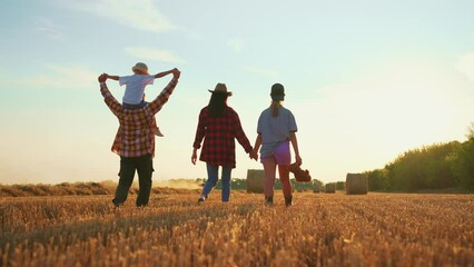 Family walking on wheat field at sunset. Happy parents children holding hands talking together in summer vacations. Farmers having fun together on farm. Farming lifestyle, relaxation, leisure concept.