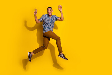 Full length photo of attractive funny guy wear print shirt running jumping high emtpy space isolated yellow color background
