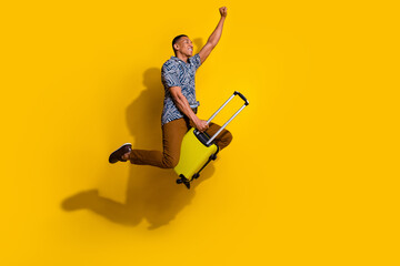 Full length photo of handsome good mood guy wear print shirt jumping riding bag empty space isolated yellow color background