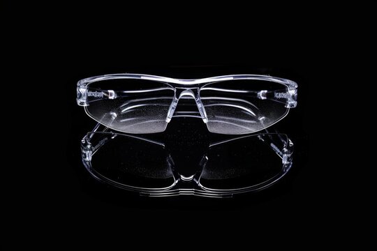 A pair of safety glasses with clear lenses reflecting light against a black background, emphasizing the importance of eye protection in construction