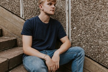 Blond man in navy blue tee sitting on stairs