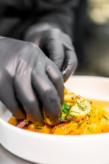 A chef in black gloves meticulously garnishes a dish, adding the final touch to the culinary presentation