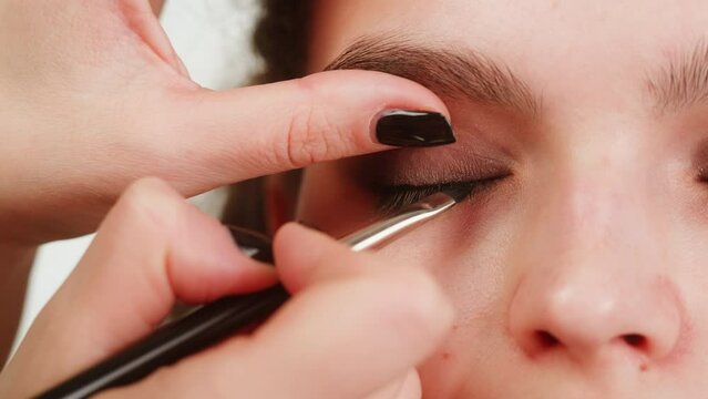 Eye shadow makeup to the upper eyelid, close-up. Makeup artist applies a bright eye shadow with a make-up brush.Tutorial master class of professional makeup, smoky eyes 