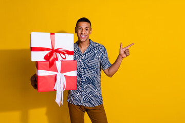 Photo of attractive funny guy wear print shirt getting new year present pointing emtpy space isolated yellow color background