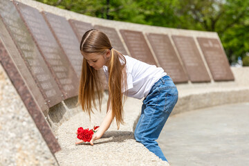 The memory of soldiers in Great Patriotic War. Little girl laying red carnations at the monument to fallen soldiers in world War II. Victory Day on May 9.