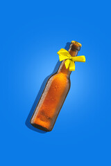 Cold, frosty beer bottle with a bright yellow bow against blue background. Contemporary art collage. Concept of alcohol drink, surrealism, celebration, creativity