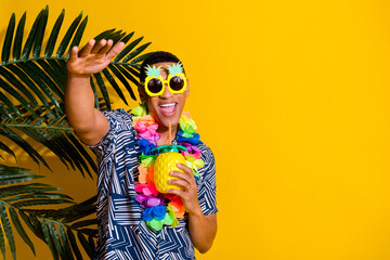 Photo of attractive funny guy wear print shirt hawaii necklace enjoy fruit juice dancing emtpy space isolated yellow color background - obrazy, fototapety, plakaty
