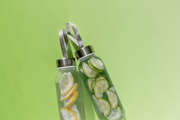 Top view two glass bottles, water drink detox with lemon and cucumber at sunlight on green, copy...