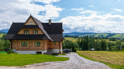 Fototapeta na wymiar What a view the owner of this wooden house just outside Dzianisz, Poland, has: Green fields, small mountains, woods, and clouds on a blue, summer sky.
