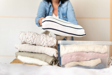 Woman stores or takes out winter sweaters from a box. Concept change of season in clothes closet
