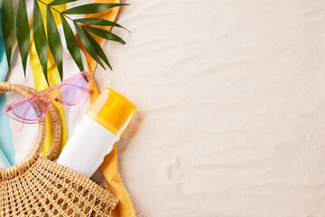 Top view of essential beach items including sunscreen, sunglasses, and a straw bag on a colorful...