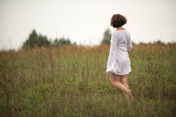 In summer, a woman in a white dress walks across a field.