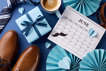 Elegant setup for Father's Day featuring a calendar, sophisticated men's accessories, and a coffee cup on a dark blue background, perfect for holiday promotions - obrazy, fototapety, plakaty