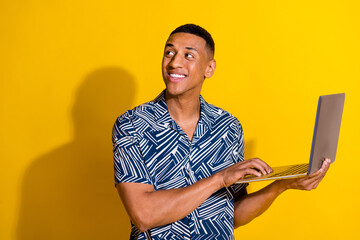 Photo of handsome good mood guy wear print shirt texting modern gadget looking emtpy space isolated yellow color background