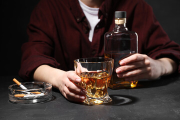 Alcohol addiction. Woman with whiskey and smoldering cigarettes at dark textured table, closeup
