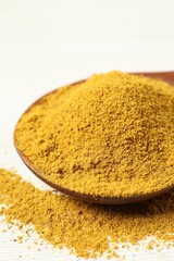 Curry powder in spoon on white wooden table, closeup