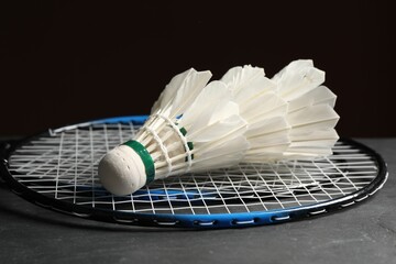 Feather badminton shuttlecocks and racket on grey table against black background, closeup