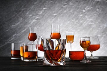 Different delicious liqueurs in glasses on dark wooden table