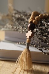 Rosary beads, books and willow branches on table, closeup