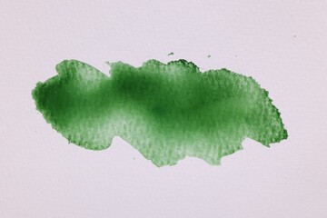 Blot of green watercolor paint on white paper, top view